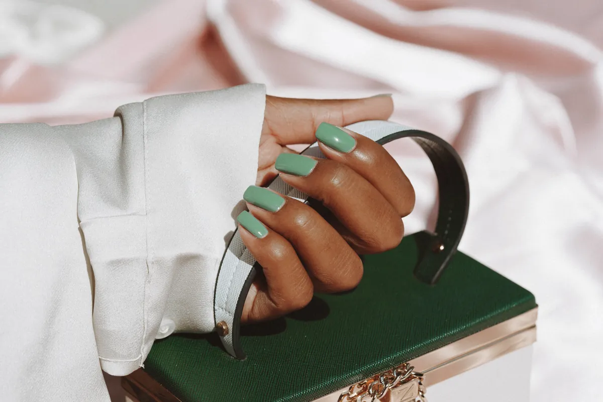 Hand with mint nails holding a plain green bag on silk