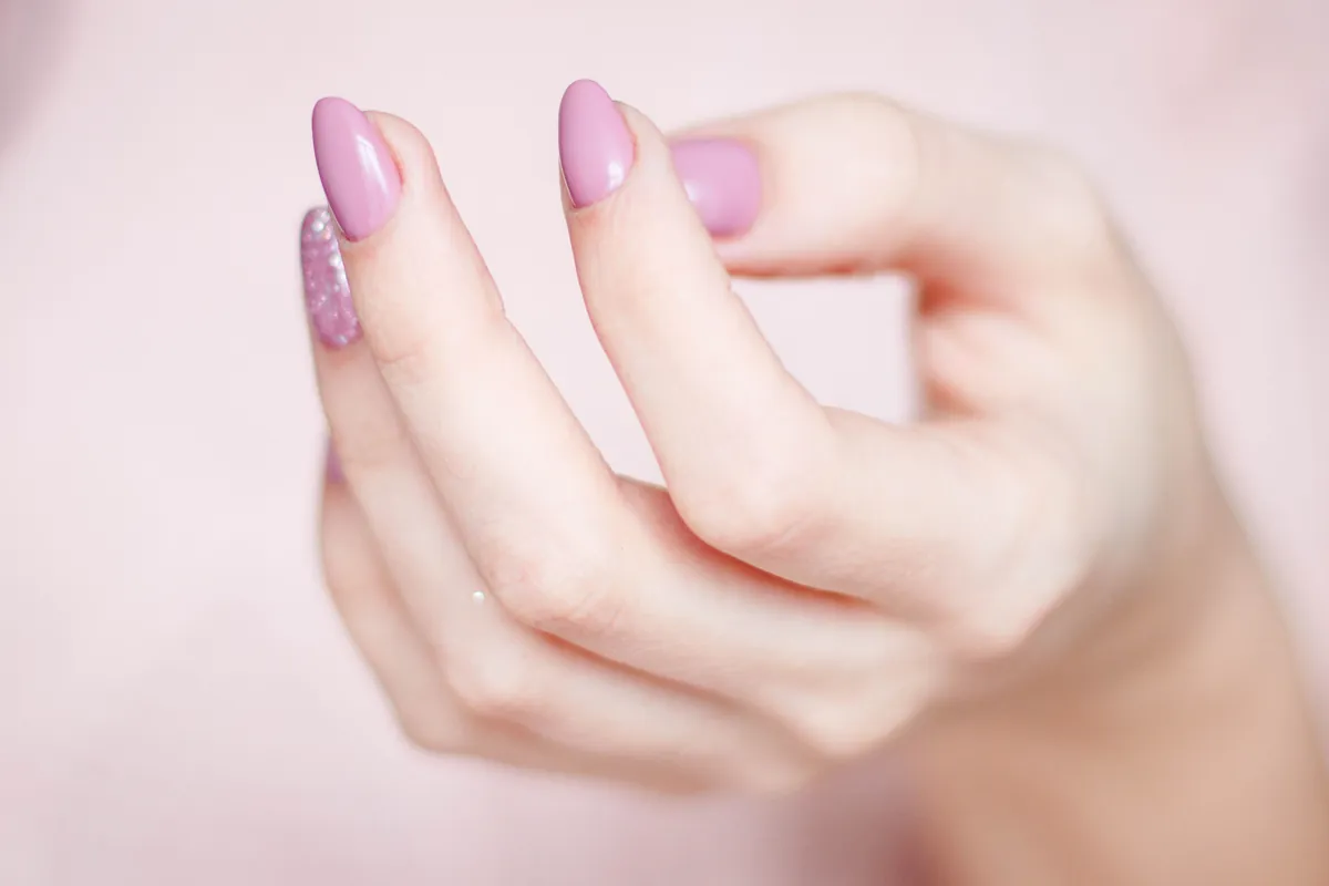 Hand with soft pink nails on pink fabric
